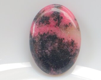 Puede incluir: Gema de forma ovalada con superficie pulida. La piedra presenta una mezcla de colores rosa, negro y blanco. El tono rosa domina la parte superior, pasando a negro en la base. La gema probablemente se utiliza en joyería.
