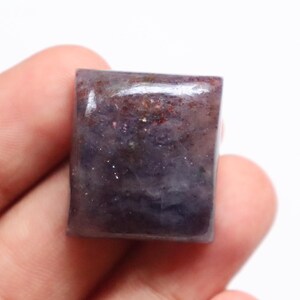 May include: A dark purple and grey gemstone cabochon with a rectangular shape. The gemstone has a smooth, polished surface and is set in a bezel setting.