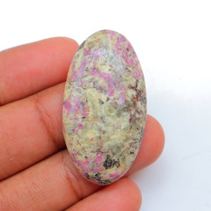 Peut inclure: Pierre précieuse de forme ovale cabochon avec un motif marbré rose et blanc. La pierre a une texture brute et naturelle.