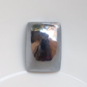 May include: A silver, rectangular, hammered metal button.