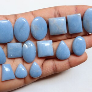 May include: A collection of 15 light blue gemstone cabochons in various shapes, including oval, square, and pear. The stones are smooth and polished, with a subtle shimmer.