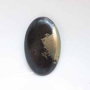 Pode incluir: Uma pedra preciosa oval de cabochão preta e dourada com uma superfície lisa e polida.