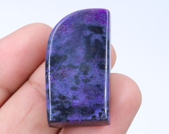 Op de afbeelding: Een paarse en zwarte cabochon edelsteen met een afgeronde bovenkant en een platte onderkant. De edelsteen is ongeveer 5 cm lang en 2,5 cm breed.