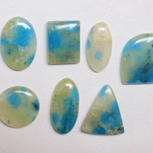 May include: Eight cabochon gemstones with a light green and blue marbled pattern. The stones are oval, rectangular, round, and triangular in shape.