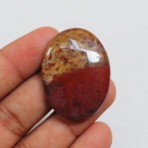 Puede incluir: Una piedra preciosa ovalada en cabujón con un acabado pulido. La piedra preciosa mide aproximadamente 5 cm de largo y 2,5 cm de ancho y presenta colores rojo, marrón y amarillo.
