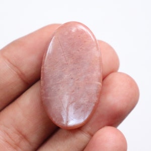 May include: A smooth, oval-shaped, pink sunstone cabochon with a light pink hue and a subtle shimmer.