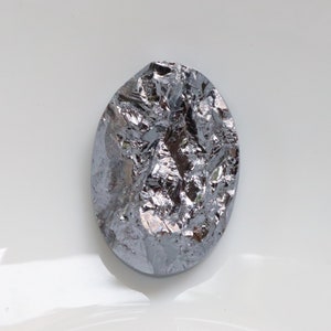 May include: A silvery gray, irregularly shaped piece of silicon, a semiconductor material, on a white background.