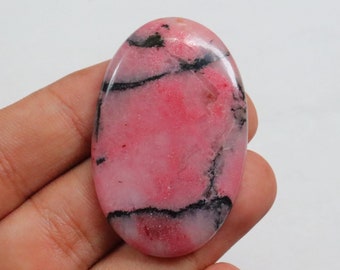Puede incluir: Una piedra preciosa ovalada cabujón con un acabado pulido. La piedra es rosa con un patrón de vetas blancas y negras que se arremolinan.
