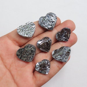 May include: Seven heart-shaped silicon wafers, each with a unique, metallic, crystalline pattern. The wafers are arranged in a hand, with the points of the hearts facing outward.