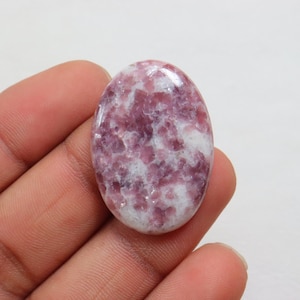 May include: Oval shaped cabochon gemstone with a white and pink color pattern. The stone has a smooth, polished surface.