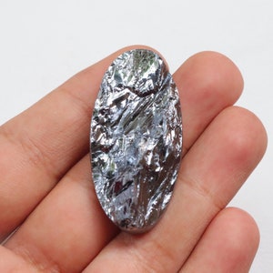 May include: A silver-colored, oval-shaped, raw, natural, gemstone with a metallic sheen. The gemstone has a rough, textured surface.