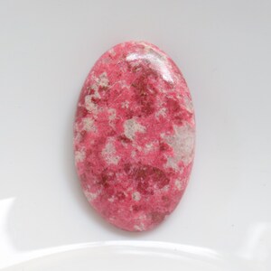 Puede incluir: Una piedra preciosa ovalada cabujón con un patrón veteado en tonos rosados y blancos.