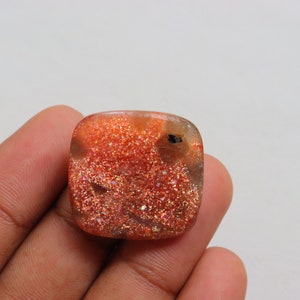 Pu&ograve; includere: Un cabochon di pietra di sole arancione di forma quadrata con una finitura scintillante e iridescente.