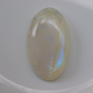 K&ouml;nnte beinhalten: Ein wei&szlig;er ovaler Mondstein-Cabochon mit schillernden blauen und violetten Blitzen.