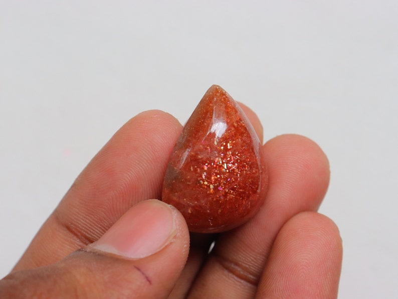 Pu&ograve; includere: Un cabochon di pietra di sole a forma di lacrima, di colore rosso-arancione e con una finitura scintillante e iridescente.