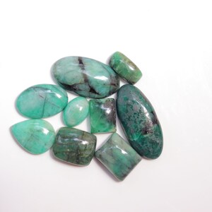 May include: A collection of eight green emerald gemstones of various shapes and sizes. The gemstones are cut and polished, and they have a translucent appearance.