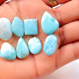 May include: A collection of eight blue and white gemstone cabochons in various shapes, including oval, pear, and square. The stones have a cloudy, marbled appearance.