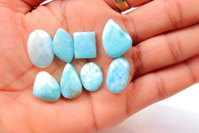 May include: A collection of eight blue and white gemstone cabochons in various shapes, including oval, pear, and square. The stones have a cloudy, marbled appearance.