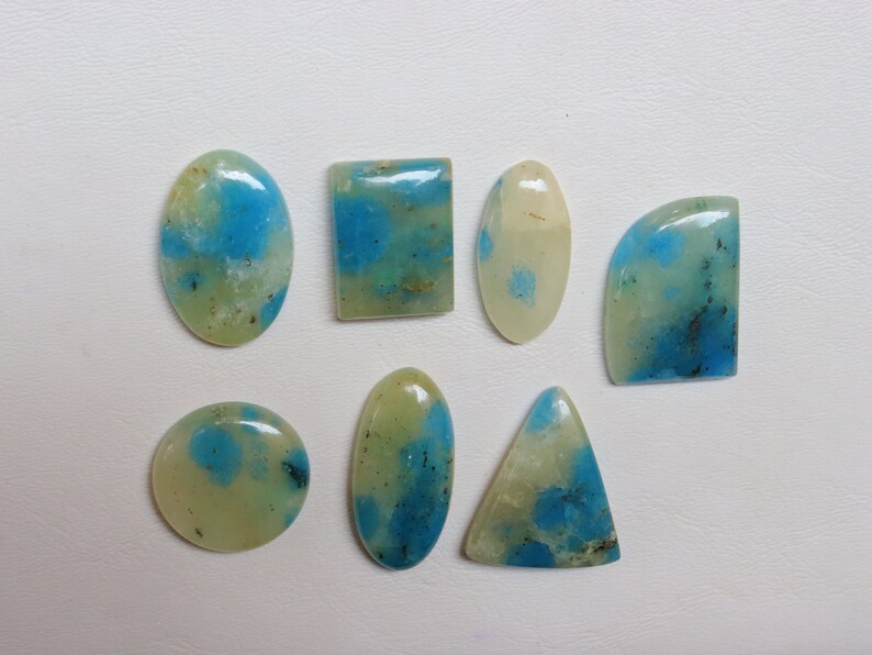 May include: Assortment of eight cabochon gemstones with a green and blue marbled pattern. The stones are various shapes, including oval, round, square, and triangular.