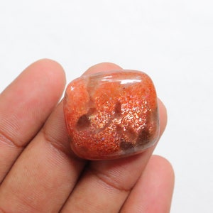 Pu&ograve; includere: Un cabochon di pietra di sole di forma quadrata, di colore arancione con una finitura scintillante e iridescente. La pietra ha un aspetto traslucido con una miscela di tonalit&agrave; arancioni, marroni e dorate.