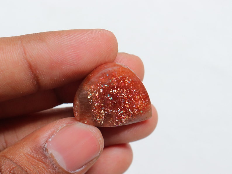 Pu&ograve; includere: Un cabochon di pietra di sole rosso, arancione e oro a forma di pera con una finitura scintillante e iridescente.