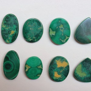Puede incluir: Ocho cabujones de malaquita verde, algunos con vetas amarillas, en forma ovalada y de l&aacute;grima.