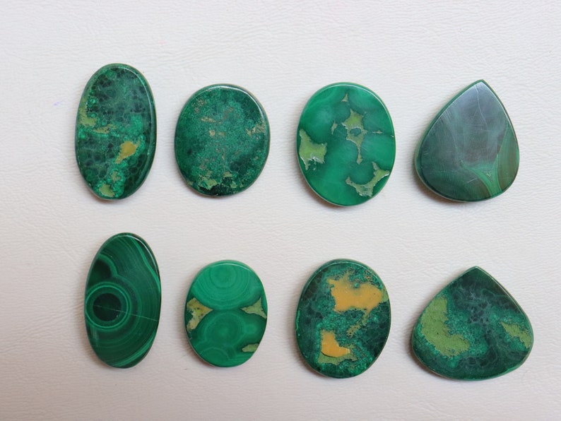 Puede incluir: Ocho cabujones de malaquita verde, algunos con vetas amarillas, en forma ovalada y de l&aacute;grima.