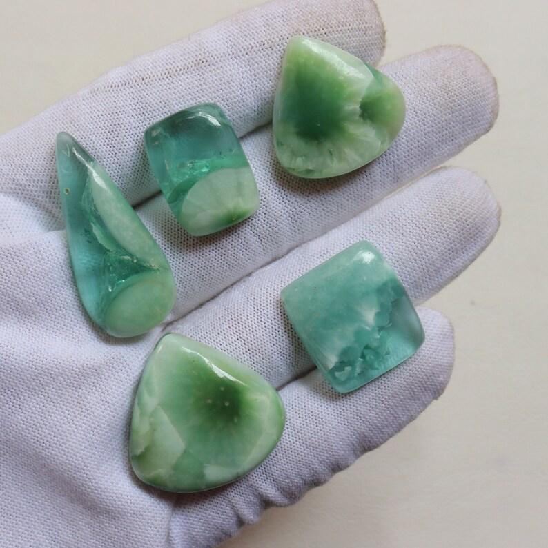 May include: Five green and blue gemstone cabochons with white inclusions. The cabochons are various shapes and sizes, including teardrop, square, and oval.