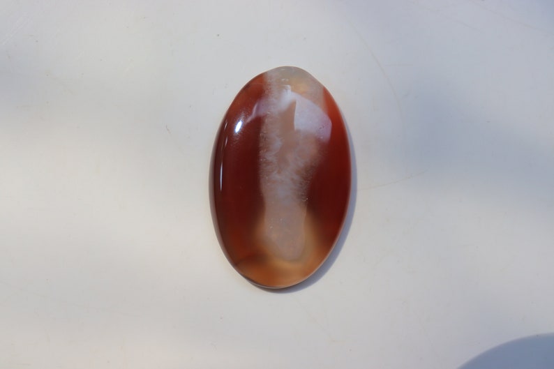 May include: A smooth, oval-shaped agate cabochon with a white and brown pattern. The stone has a glossy finish.