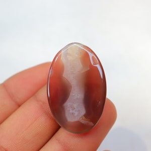 May include: A smooth, oval-shaped agate gemstone with a white and brown pattern. The stone is translucent and has a glossy finish.