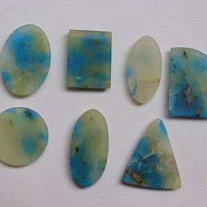 May include: Seven cabochon gemstones in various shapes and sizes, including oval, round, rectangle, and triangle. The stones are a pale yellow-green color with blue and gray inclusions.