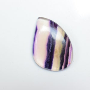 May include: A teardrop-shaped cabochon gemstone with a white, purple, and yellow striped pattern.