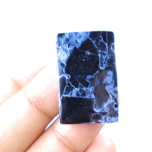 May include: A rectangular gemstone with a striking pattern of deep blue and black. The polished surface reveals a network of veins, creating a unique and eye-catching design. The stone is held against a white background.