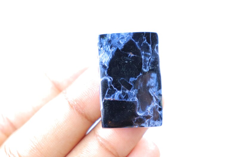 May include: A rectangular gemstone with a striking pattern of deep blue and black. The polished surface reveals a network of veins, creating a unique and eye-catching design. The stone is held against a white background.