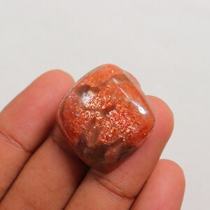 Pu&ograve; includere: Un cabochon di pietra di sole arancione traslucido di forma quadrata con una finitura scintillante e iridescente.