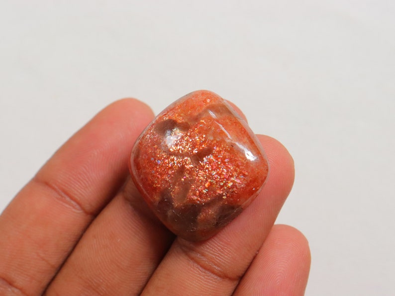 Pu&ograve; includere: Un cabochon di pietra di sole arancione traslucido di forma quadrata con una finitura scintillante e iridescente.