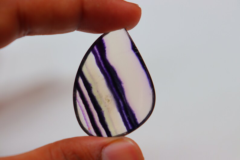May include: A teardrop-shaped, translucent purple and white fluorite gemstone with a banded pattern.