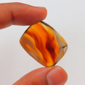 Op de afbeelding: Een rechthoekige, oranje agaat cabochon met witte en bruine banden. De steen is doorschijnend en heeft een glad, gepolijst oppervlak.