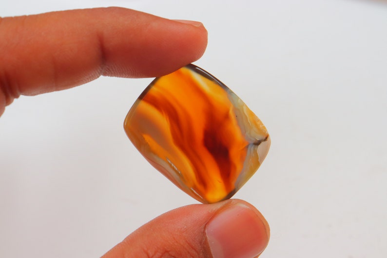 Op de afbeelding: Een rechthoekige, oranje agaat cabochon met witte en bruine banden. De steen is doorschijnend en heeft een glad, gepolijst oppervlak.