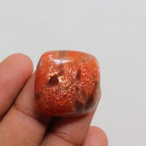 Pu&ograve; includere: Un cabochon di pietra di sole di forma quadrata, di colore arancione, con una finitura scintillante e iridescente. La pietra &egrave; traslucida con inclusiones marroni e arancioni.