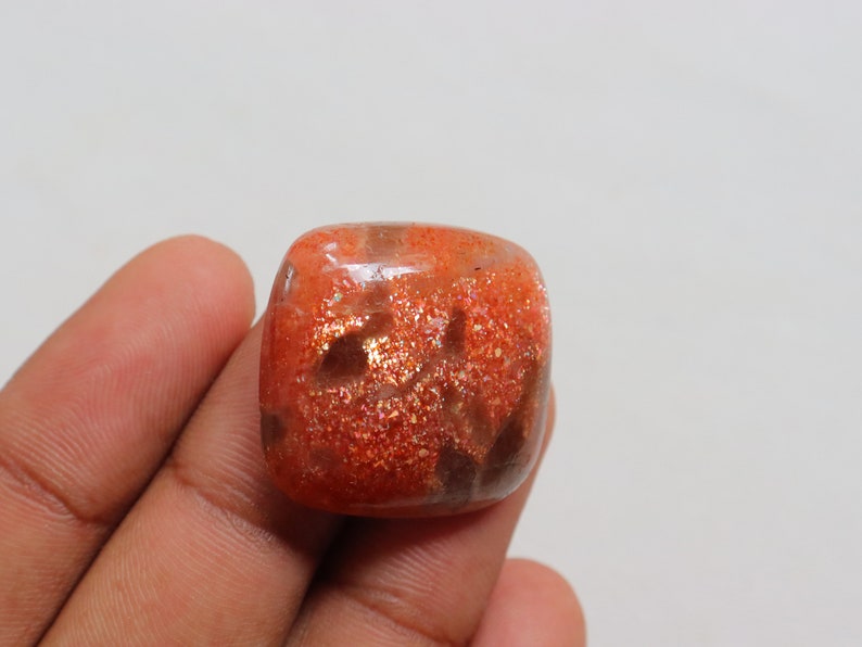 Pu&ograve; includere: Un cabochon di pietra di sole di forma quadrata, di colore arancione, con una finitura scintillante e iridescente. La pietra &egrave; traslucida con inclusiones marroni e arancioni.