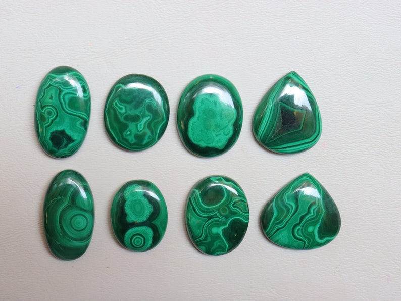 Puede incluir: Ocho cabujones de malaquita pulida en varias formas y tama&ntilde;os. Los cabujones son de color verde oscuro con intrincados patrones de vetas en espiral.