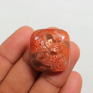 Pu&ograve; includere: Un grande cabochon di pietra di sole rettangolare di colore arancione con una finitura scintillante e iridescente. La pietra presenta una miscela di colori arancio, marrone e oro.