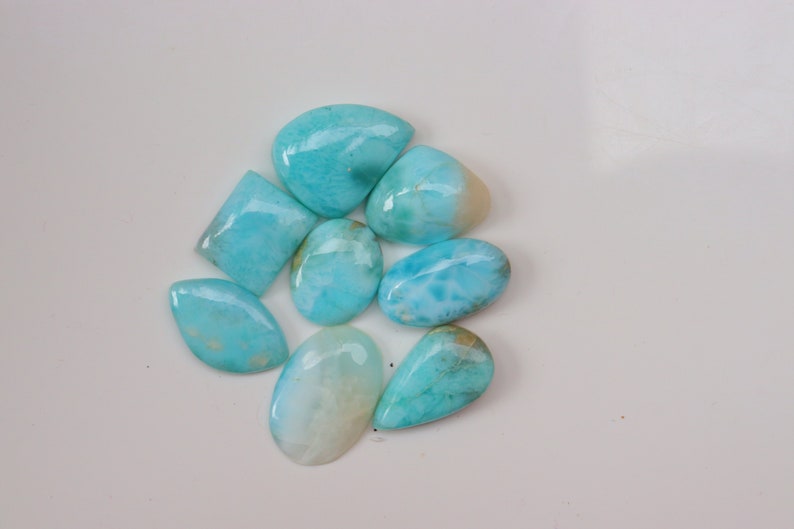 May include: A collection of eight blue and white cabochon gemstones. The gemstones are various shapes and sizes, including oval, teardrop, and square.
