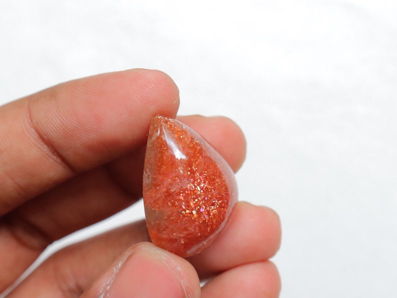 Pu&ograve; includere: Un cabochon di pietra di sole sfaccettato a forma di lacrima, di colore rosso-arancio translucido con una finitura scintillante e iridescente.