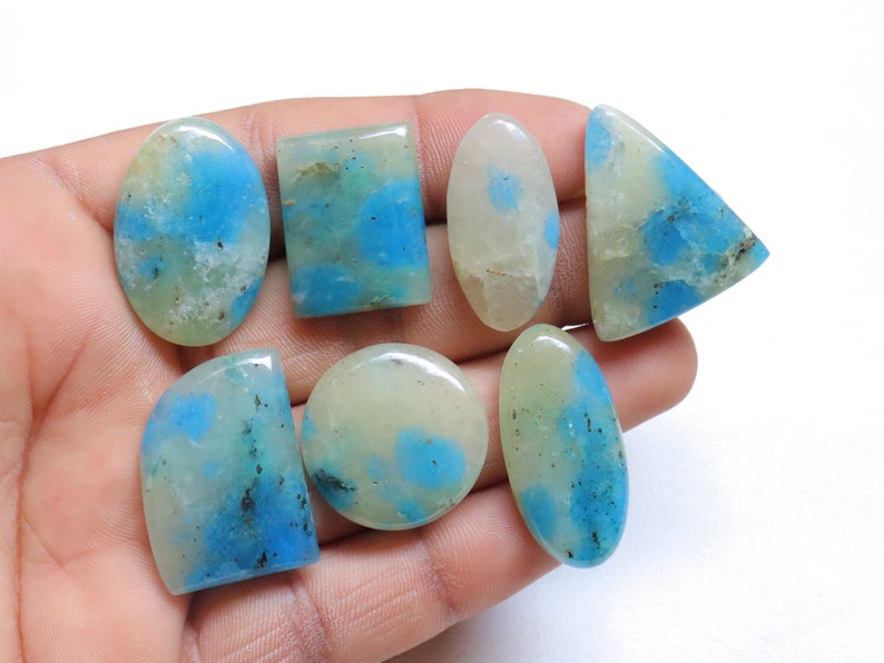 May include: Seven cabochon gemstones in various shapes and sizes, including oval, square, and triangular. The stones are a mix of white and blue with a mottled pattern.