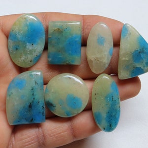 May include: Seven cabochon gemstones with a white and blue marbled pattern. The stones are various shapes and sizes, including oval, round, and rectangular.