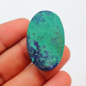 K&ouml;nnte beinhalten: Ovaler Cabochon-Edelstein mit einem gr&uuml;n-blauen Farbmuster. Der Stein hat eine raue, nat&uuml;rliche Textur.