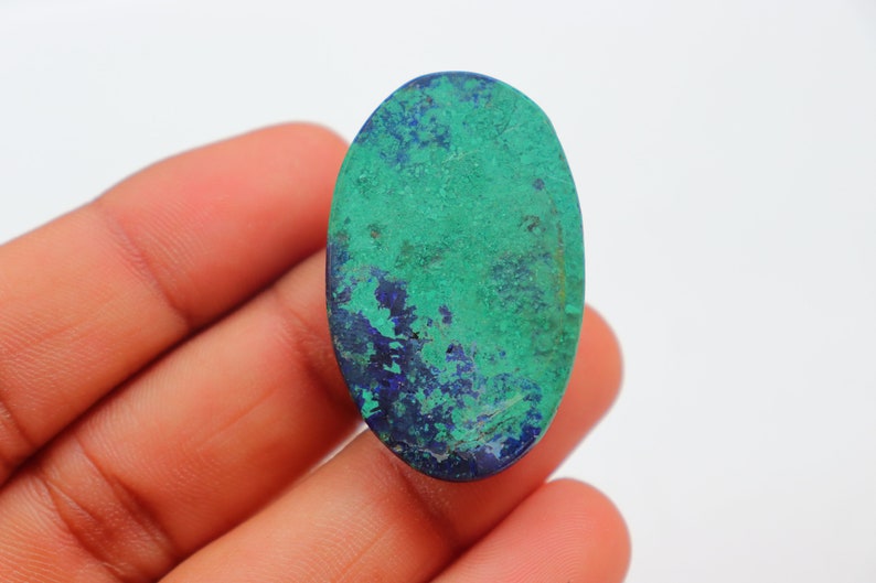 K&ouml;nnte beinhalten: Ovaler Cabochon-Edelstein mit einem gr&uuml;n-blauen Farbmuster. Der Stein hat eine raue, nat&uuml;rliche Textur.