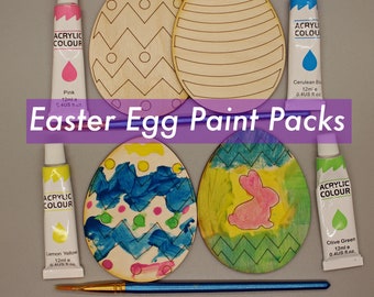 May include: An overhead shot of Easter egg paint packs. The image features wooden egg cutouts, paint tubes in pink, cerulean blue, lemon yellow, and olive green, and paintbrushes. The text "Easter Egg Paint Packs" is displayed across the image.